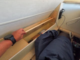 RV rental interior showing a hand with a smartwatch reaching into built-in wooden storage, alongside a sleeping area and power inverter.