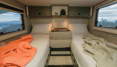 Cozy RV rental bedroom showing twin beds, overhead storage, and stunning window views.