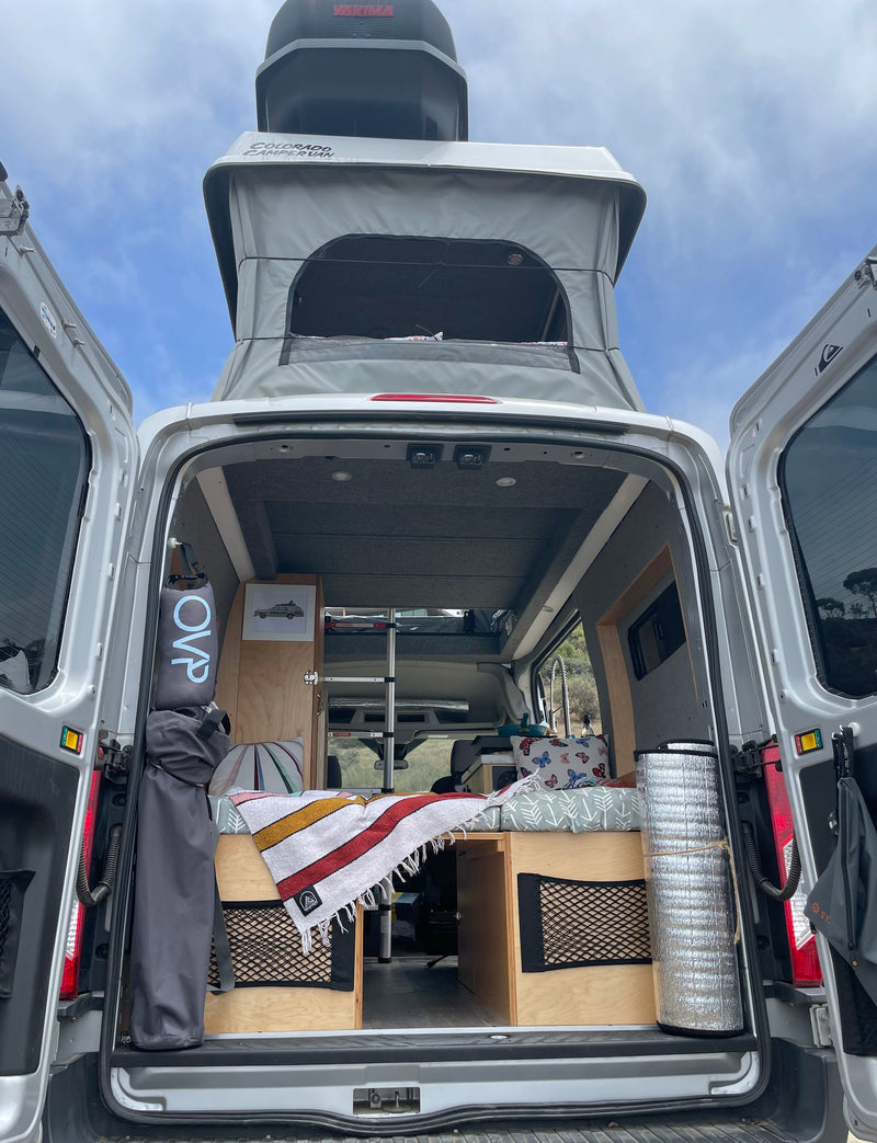 View into a custom pop-top camper van, perfect for an rv rental adventure. Features a convertible bed, kitchen, and storage. — photo 14