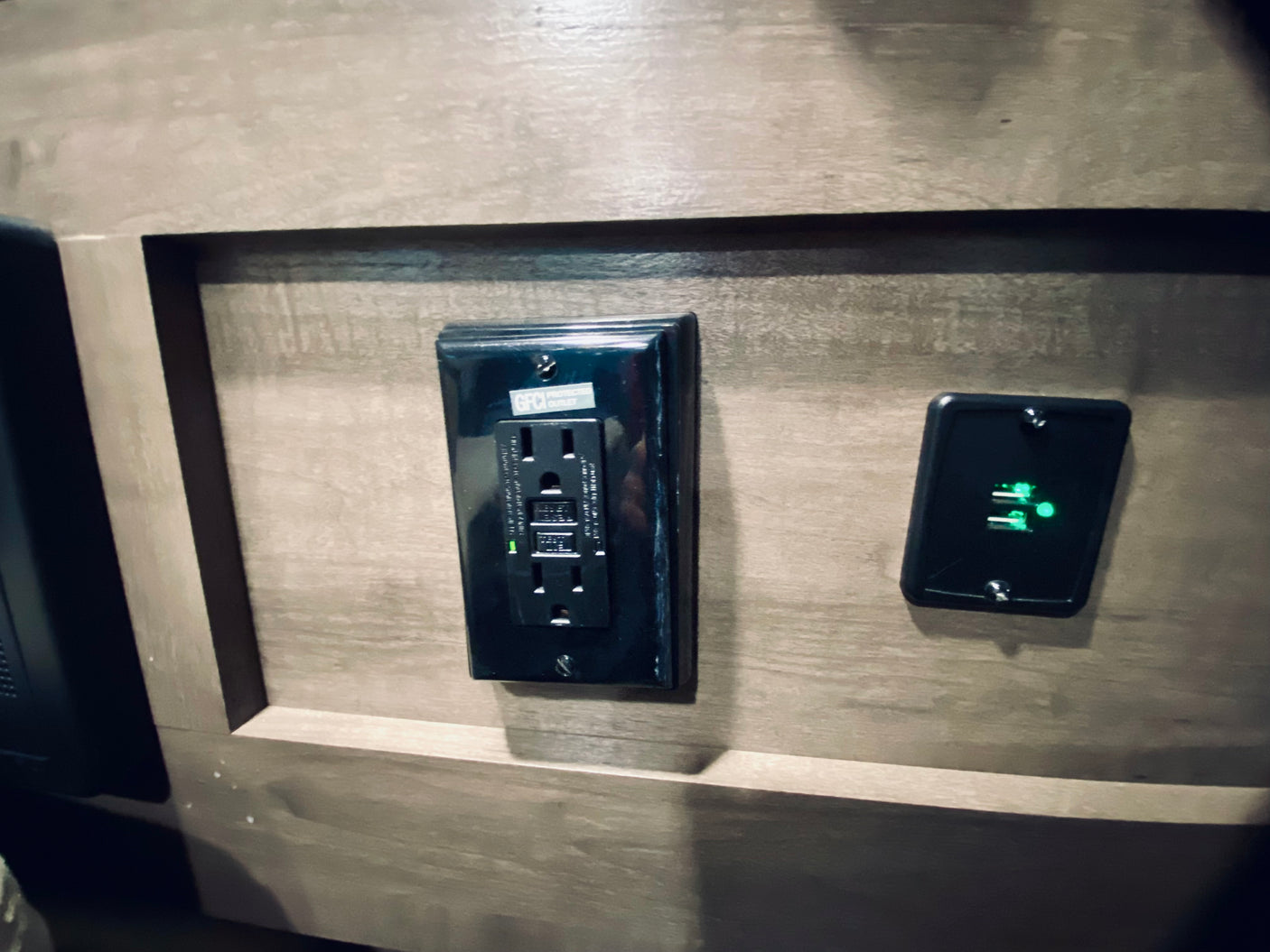 Modern amenities in your rv rental: A GFCI power outlet and a dual USB charging port with green lights on a wood RV wall.