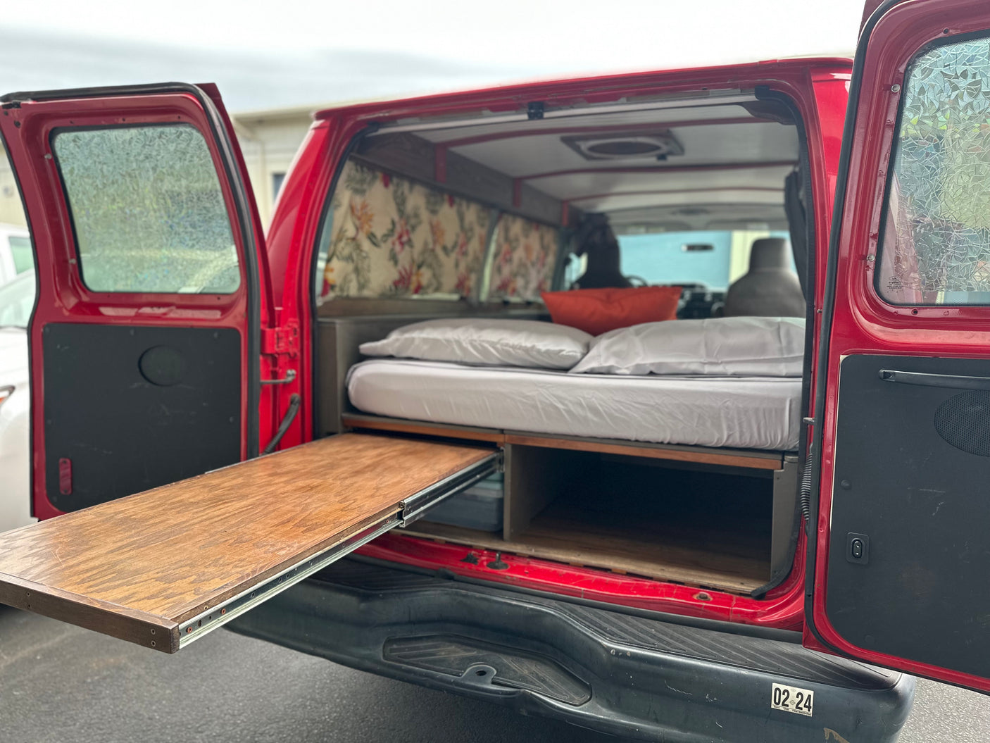 Red camper van interior with bed, storage, and slide-out table, perfect for an RV rental adventure.
