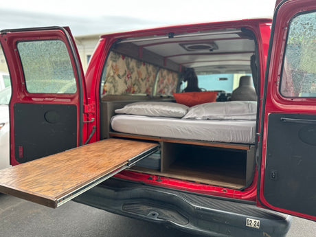 Red camper van interior with bed, storage, and slide-out table, perfect for an RV rental adventure.