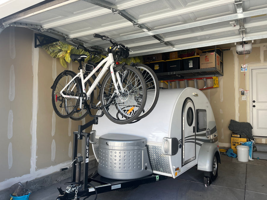 Small white RV (teardrop camper) with bikes on its front rack, neatly stored in a garage, perfect for an rv rental.