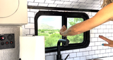 Modern RV rental kitchen: white subway tiles, black faucet, power panel, and a scenic window view.