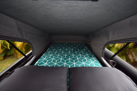 Enjoy this RV rental pop-top camper interior: a comfy bed with a geometric pattern & stunning nature views.