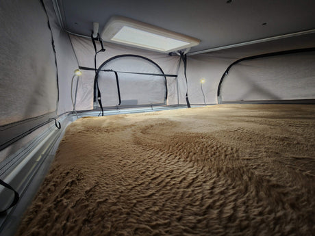 Cozy RV rental interior with a fluffy bed, bright light, and pop-top fabric walls, offering a comfortable space.