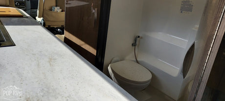 This RV rental interior shows a modern kitchen counter with a cooktop, and a compact bathroom with a toilet and shower.