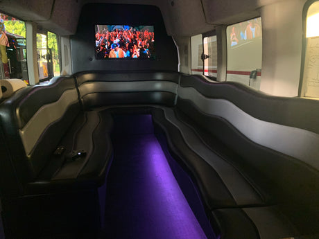 Spacious RV rental interior with black & grey lounge seats, large screen, and vibrant purple floor lighting.