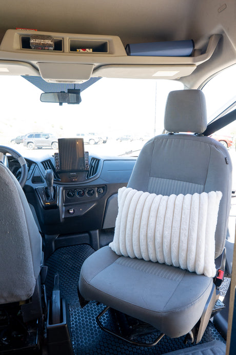 Inside an RV rental van: cozy passenger seat with a pillow, detailed dashboard, and overhead storage for a comfortable journey.