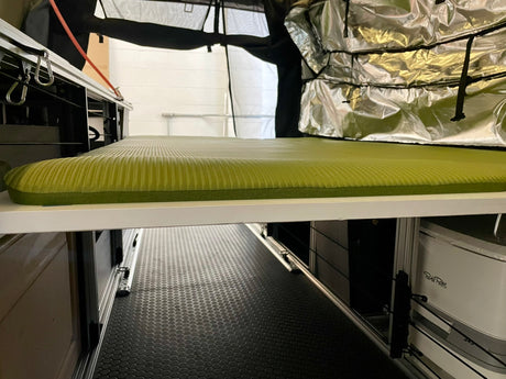 Compact RV rental interior featuring a comfortable sleeping pad, under-bed storage, and a portable Porta Potti for adventure travel.