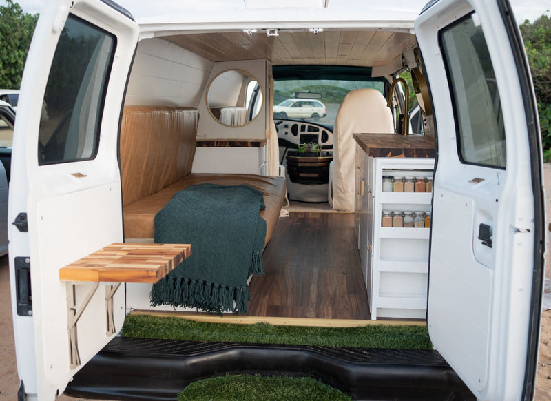  and pull-out spice rack.|Hand pulls out a sleek gold faucet head in an RV rental kitchen with wood counters. Modern features enhance your travels.|A white conversion van with a cat peeking from the window — photo 13
