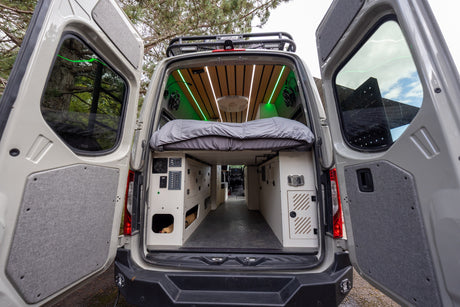 Inside an RV rental campervan: modern interior with a cozy bed, custom storage, and vibrant green LED lighting.