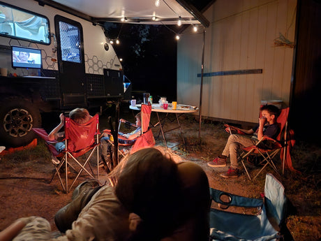 Relaxed family camping under string lights by an RV rental. Kids enjoy outdoor screen time at night.