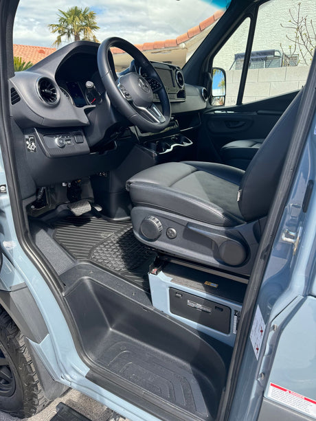 Driver's side view of a modern Mercedes Sprinter RV rental interior. Features dashboard, steering wheel, comfortable seat, and floor.
