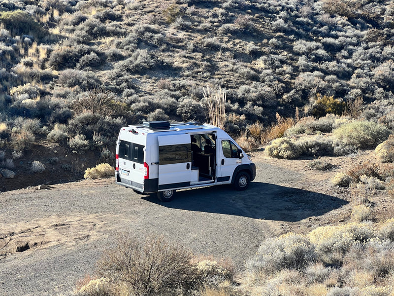 White RV rental camper van parked on a dirt road in a sunny, scrub-covered desert landscape. Side door open for exploring. — photo 3