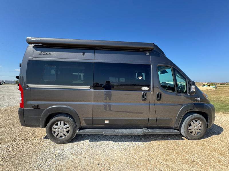 Dark gray Scope camper van with a Thule awning on a gravel lot under a blue sky. A perfect rv rental for adventure. — photo 2