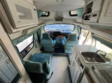 Interior view of an RV rental, featuring a well-equipped kitchen (sink, microwave), comfortable blue seating, and front driving area.