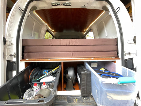 This RV rental's camper van interior showcases a cozy, foldable bed atop smart storage for all your travel gear.