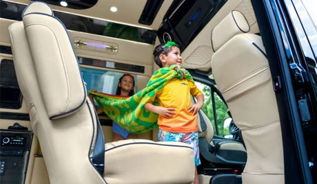 Family adventure in an RV rental: A boy in a towel cape stands proudly in a luxury van; a girl smiles behind him.
