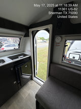 Inside a modern RV rental: compact kitchen with sink/cooktop, fridge, and cozy seating area. Door open to outside.