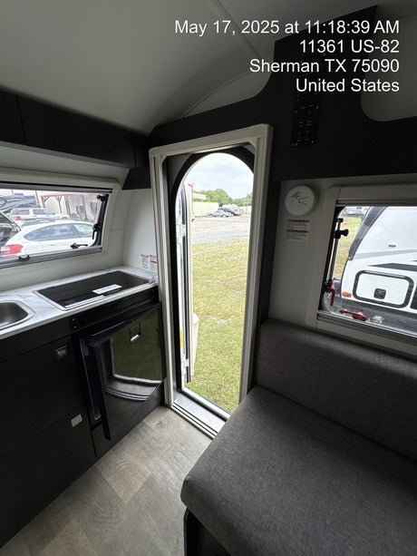 Inside a modern RV rental: compact kitchen with sink/cooktop, fridge, and cozy seating area. Door open to outside.