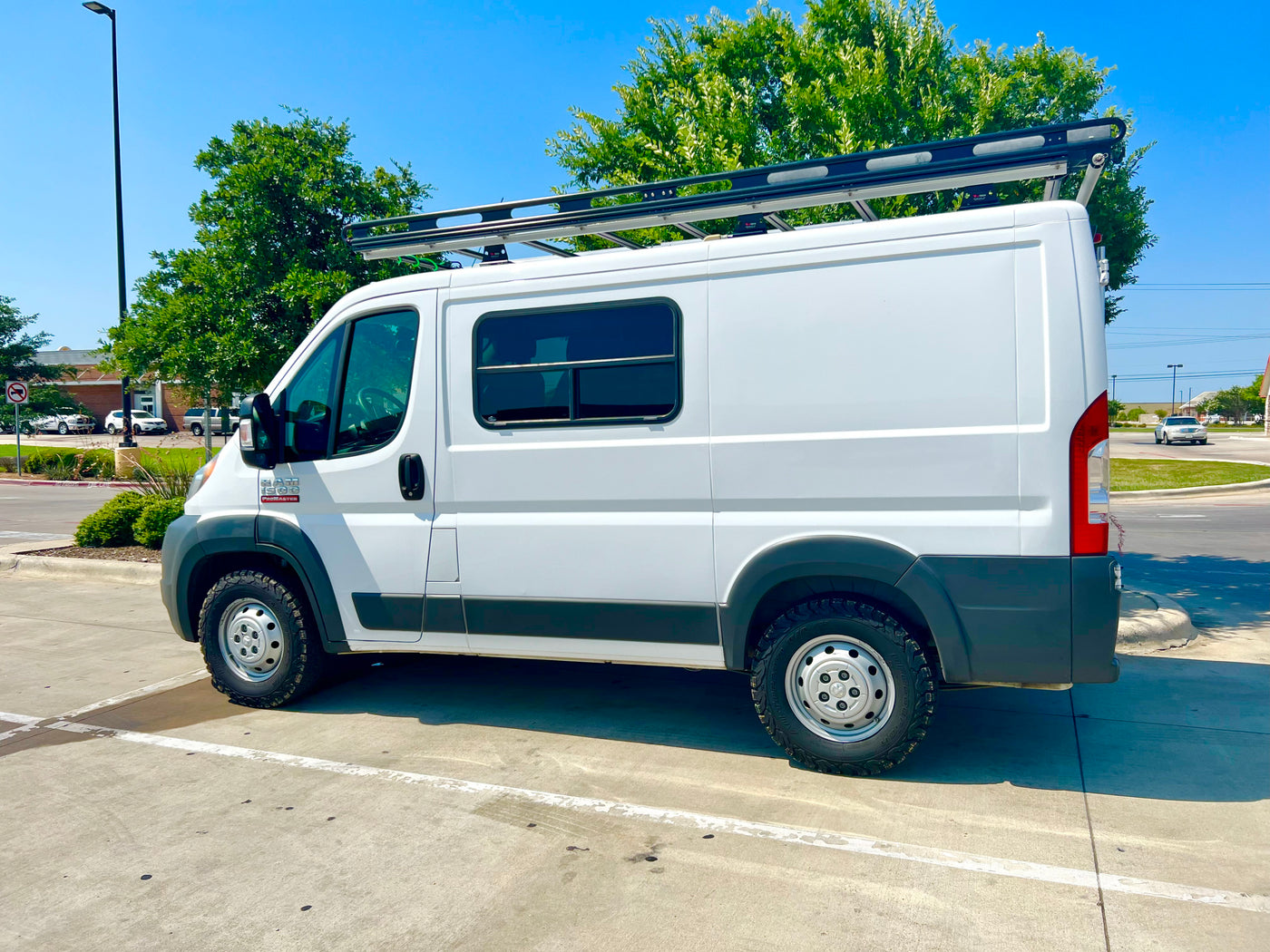 A white Ram ProMaster camper van with a roof rack and all-terrain tires, ready for an rv rental journey. — photo 11