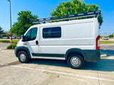 A white Ram ProMaster camper van with a roof rack and all-terrain tires, ready for an rv rental journey.
