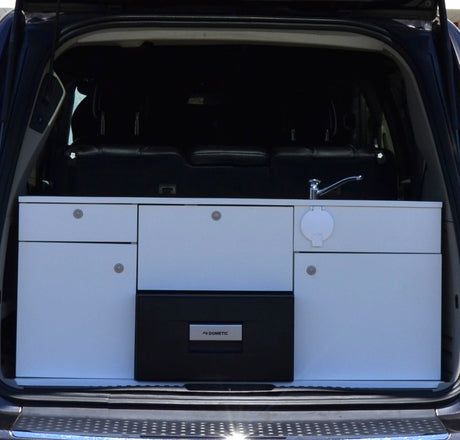 RV rental: A vehicle's trunk holds a compact camper kitchen module with sink, faucet, drawers, and Dometic fridge.