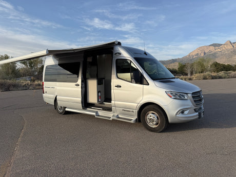 Silver Pleasure-Way Plateau-FL Mercedes-Benz Sprinter rv rental with open door & extended awning, parked with mountains.