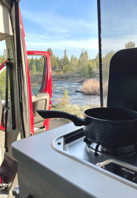 RV rental: Cooking with a view! Pot on stove inside, open van door reveals a serene river and forest.