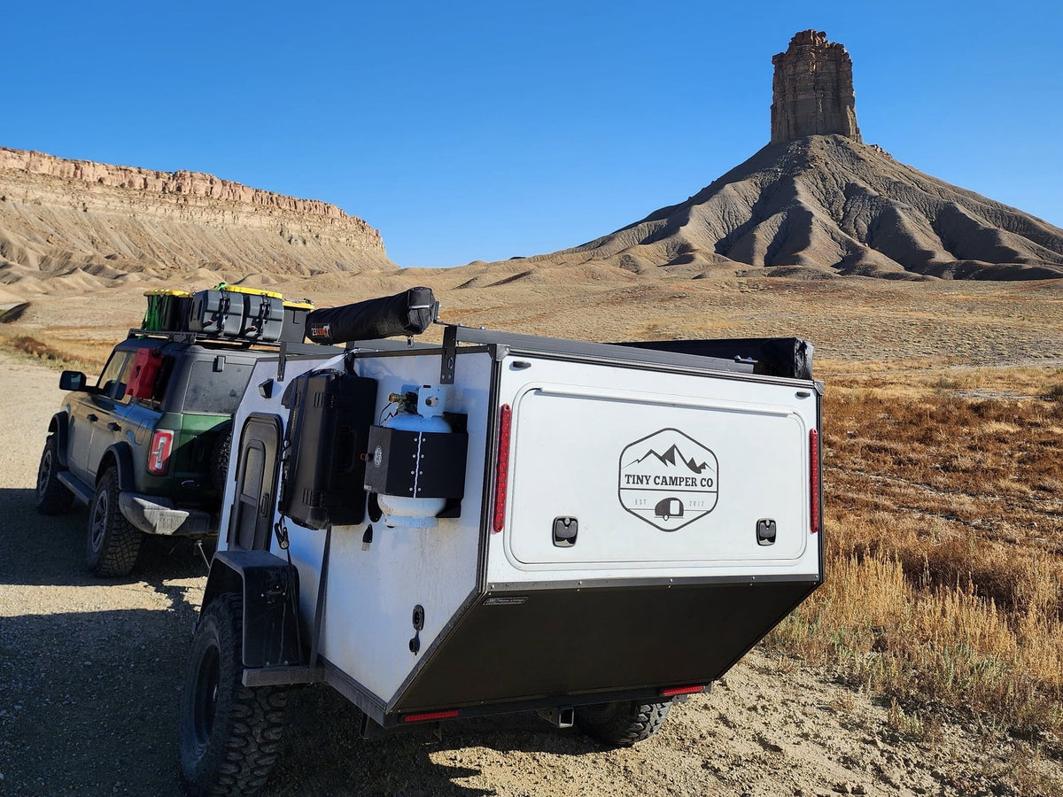 An off-road rv rental adventure with a Bronco towing a Tiny Camper Co trailer through a vast desert with towering mesas.|Inside a compact RV rental: features a comfortable bed — photo 1