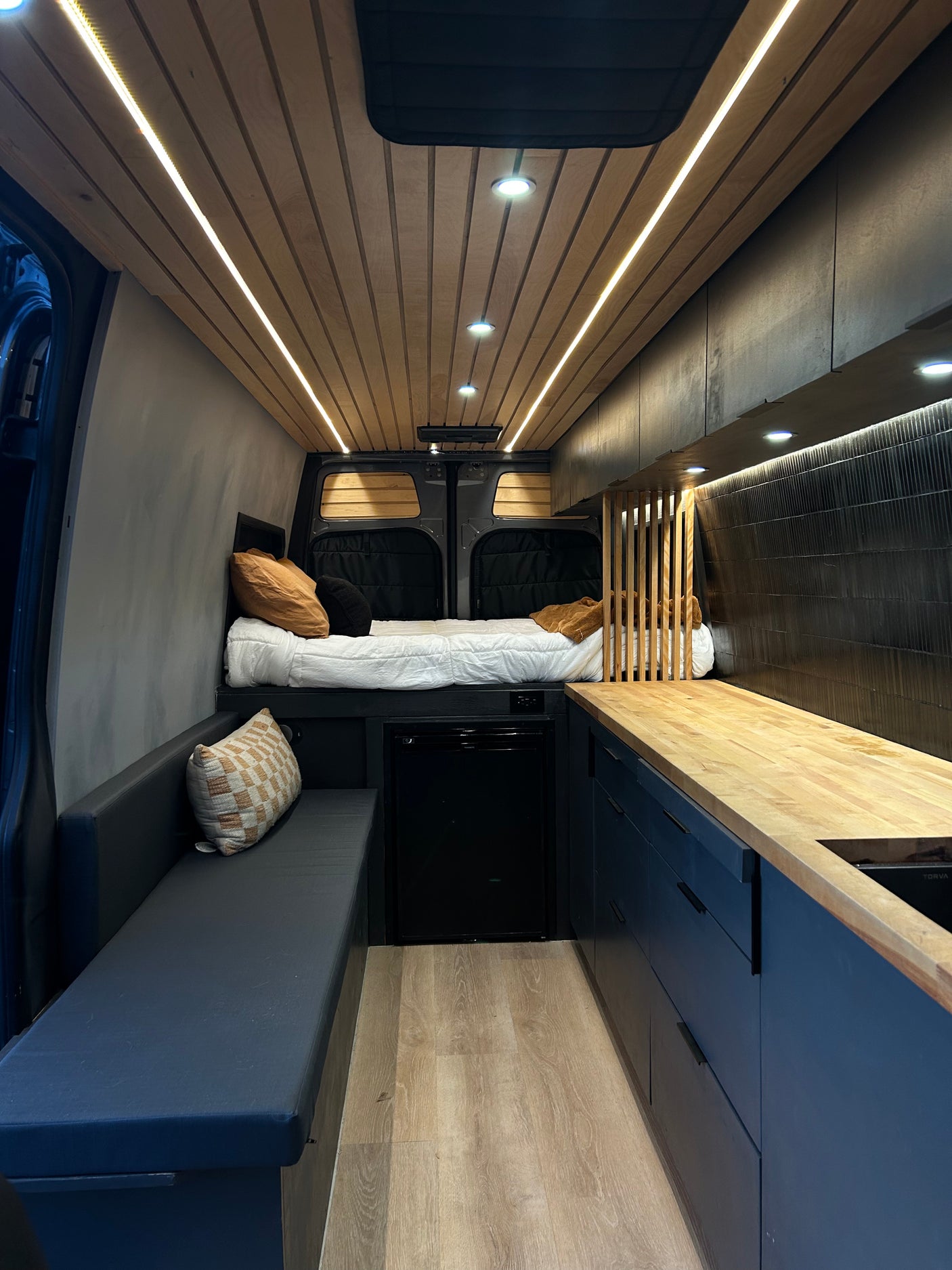 Modern camper van RV rental interior featuring a bed, kitchen, and seating area with warm lighting, ideal for travel.