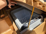 Inside a custom RV rental, an open portable refrigerator displays 9.4°C. A hand opens the lid, revealing essential camp storage.