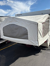 Palomino pop-up RV rental with canvas extension and mesh windows, parked on asphalt under a blue sky.