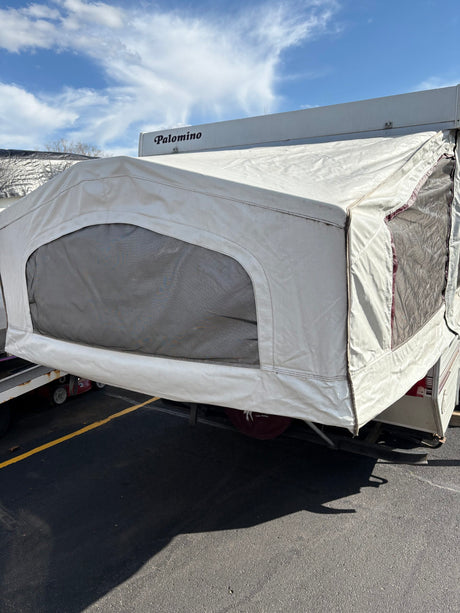 Palomino pop-up RV rental with canvas extension and mesh windows, parked on asphalt under a blue sky.