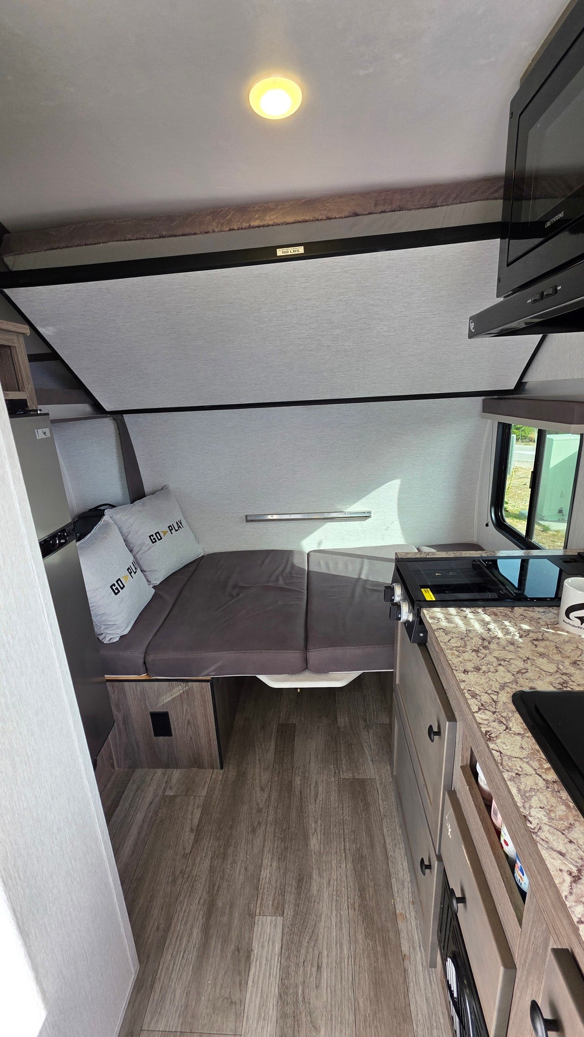 Compact rv rental interior shows a bed, kitchen with stovetop & microwave, plus a 100-lb capacity bunk. Ready for adventure! — photo 10