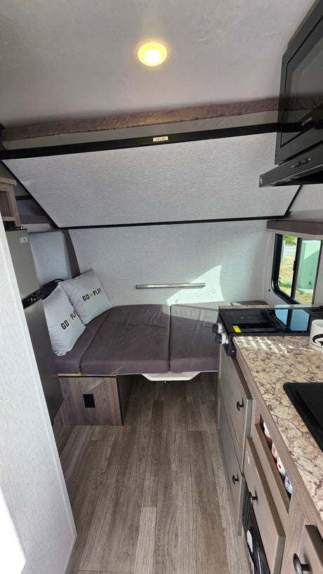 Compact rv rental interior shows a bed, kitchen with stovetop & microwave, plus a 100-lb capacity bunk. Ready for adventure!