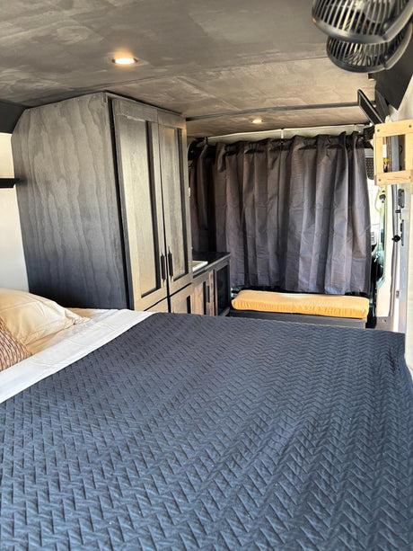 Inside this **RV rental**, see a modern camper van setup: comfy bed, dark cabinets, and kitchen area. Ideal for travel.
