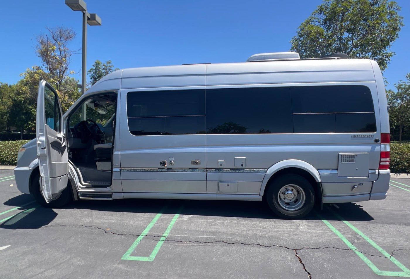  parked under a bright sky. Building in the background.|Silver Mercedes-Benz Sprinter RV rental parked on a sunny day with the driver's door open.|Spacious RV rental interior with white leather seats — photo 5