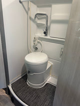 Compact white RV rental bathroom with a toilet, integrated shower faucet, and controls on a dark mat.