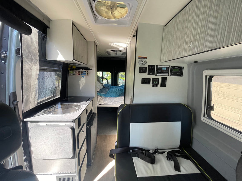 Explore this modern RV rental interior featuring a compact kitchen, comfortable bed, and accessible control panels for your adventure. — photo 5