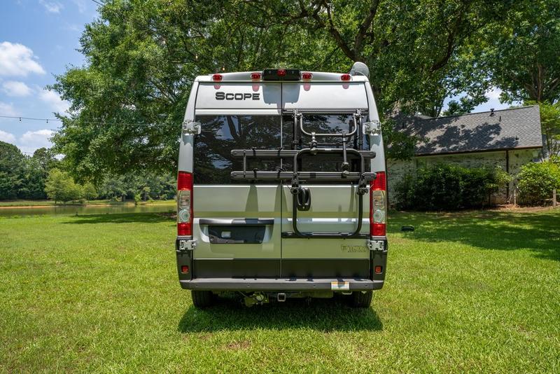 Rear view of a silver camper van RV rental with a bike rack, parked in a sunny, grassy field by a lake. — photo 6