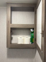 Open medicine cabinet in an RV rental bathroom, showing toilet paper and cleaning supplies on a shelf.