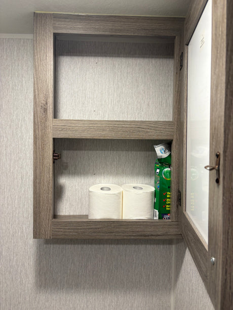 Open medicine cabinet in an RV rental bathroom, showing toilet paper and cleaning supplies on a shelf.