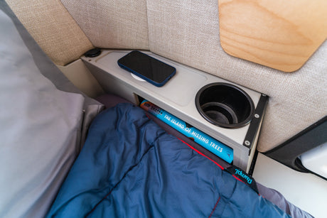 Cozy rv rental bunk: a sleeping bag, phone, book, and cup holder in an organized interior.