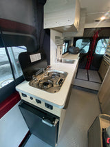 Explore the compact and functional interior of an RV rental camper van, featuring a kitchenette with a sink, stove, and fridge.