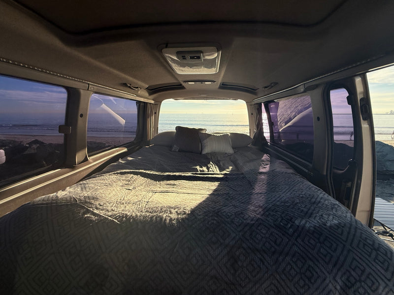  and cornhole outside by the ocean.|This RV rental offers a cozy campervan interior with a bed — photo 4