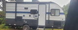 Side view of a gray and blue travel trailer, an RV rental unit. It has a prominent door, windows, and outdoor speakers.