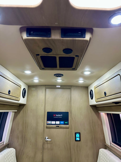 Interior of a luxurious rv rental, featuring a TV, overhead lights, storage, and plush seating for a comfortable travel experience.