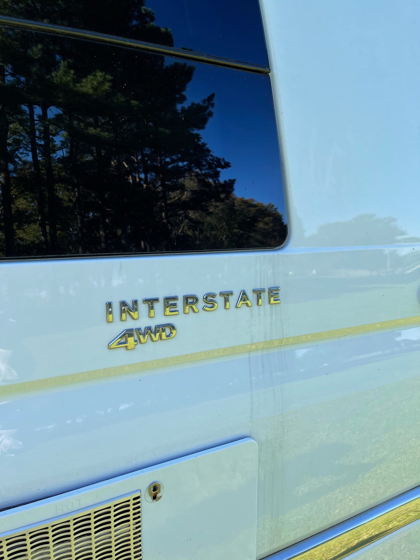 Side view of an Interstate 4WD RV, likely an rv rental, with a tinted window reflecting trees and a utility panel below. — photo 5